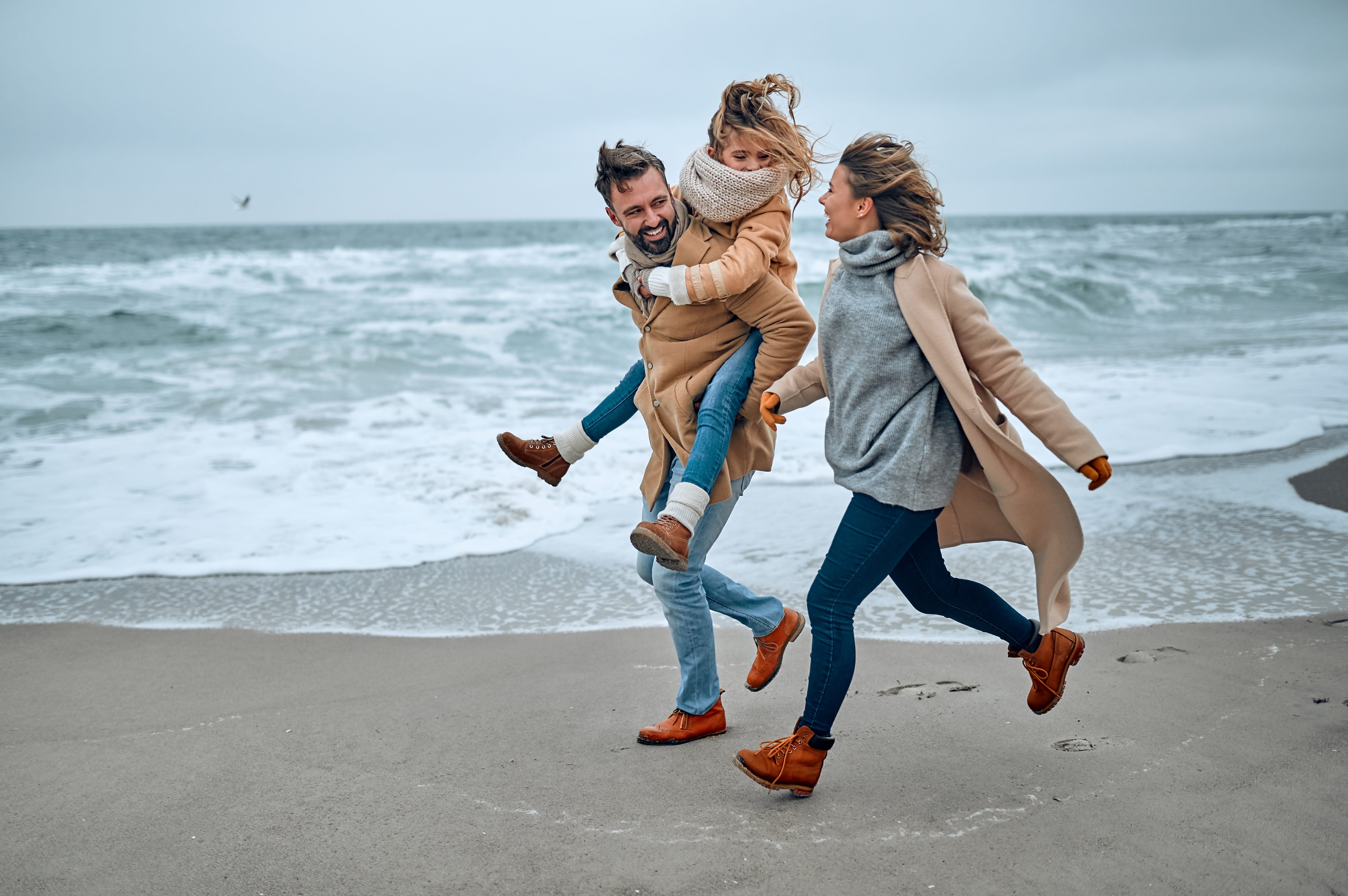 Family running on the beach during fall.